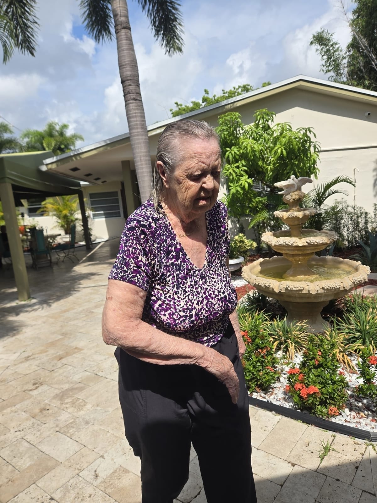 A resident walking the garden path by the fountain at Royal Palm Senior Residence.
