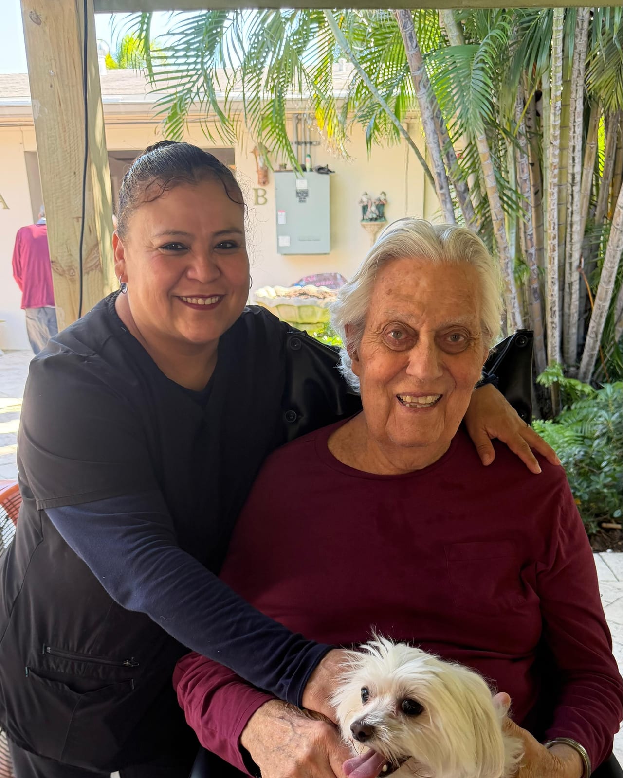 A caregiver and resident with a visiting dog outdoors at Royal Palm.